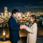 夜景の前で夫が妻にプレゼントを渡す